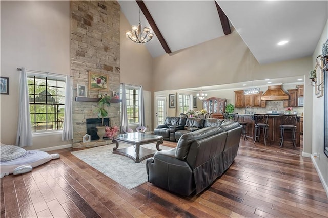 living room with dark hardwood / wood-style flooring, an inviting chandelier, high vaulted ceiling, and a stone fireplace