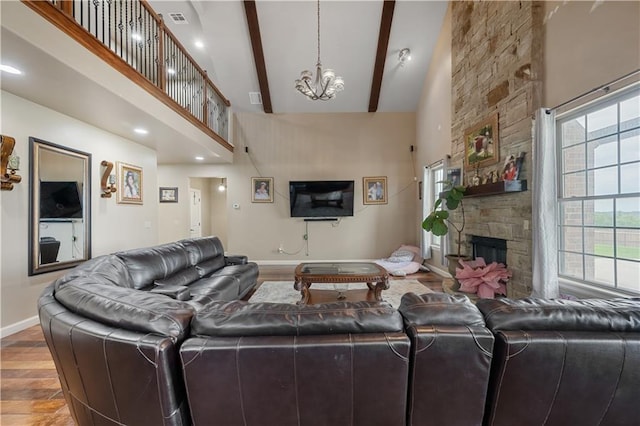 living room with beam ceiling, wood-type flooring, high vaulted ceiling, a notable chandelier, and a stone fireplace