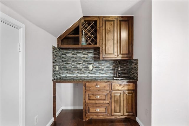 bar featuring lofted ceiling, backsplash, dark stone counters, sink, and dark hardwood / wood-style flooring