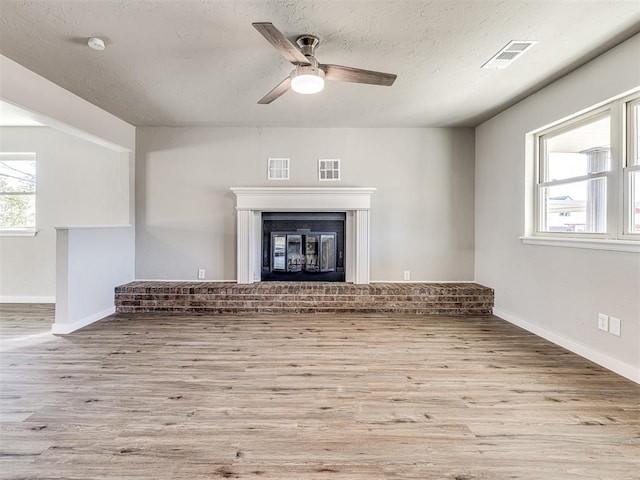 unfurnished living room featuring ceiling fan, a fireplace, a textured ceiling, and light wood-type flooring