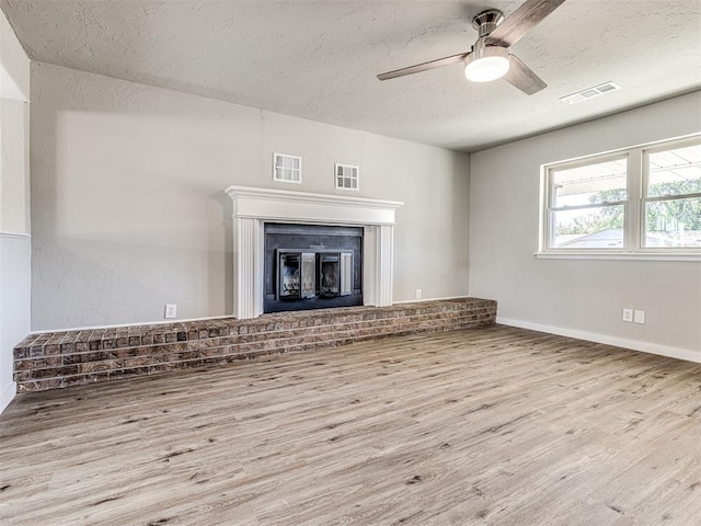 unfurnished living room featuring a brick fireplace, a textured ceiling, light hardwood / wood-style flooring, and ceiling fan