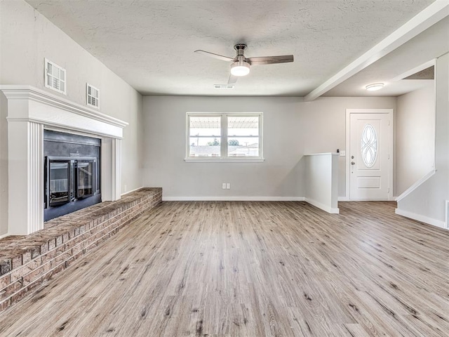 unfurnished living room with a brick fireplace, ceiling fan, a textured ceiling, beamed ceiling, and light hardwood / wood-style floors