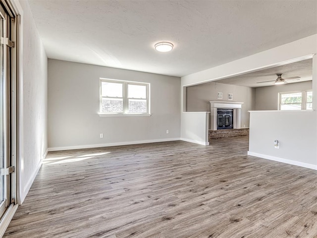 unfurnished living room with a textured ceiling, light wood-type flooring, a brick fireplace, and ceiling fan