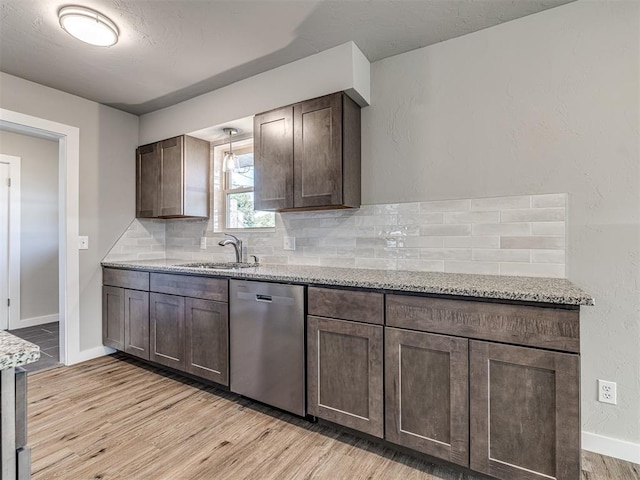 kitchen with light wood-type flooring, backsplash, light stone counters, sink, and dishwasher