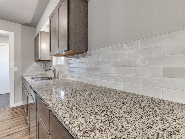 kitchen with light wood-type flooring, backsplash, light stone counters, dark brown cabinets, and sink