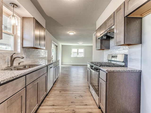 kitchen with light stone countertops, appliances with stainless steel finishes, light wood-type flooring, extractor fan, and sink