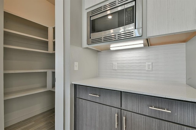 kitchen with gray cabinets, light stone counters, stainless steel microwave, and hardwood / wood-style floors