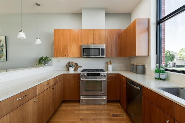 kitchen with decorative backsplash, appliances with stainless steel finishes, kitchen peninsula, dark wood-type flooring, and pendant lighting