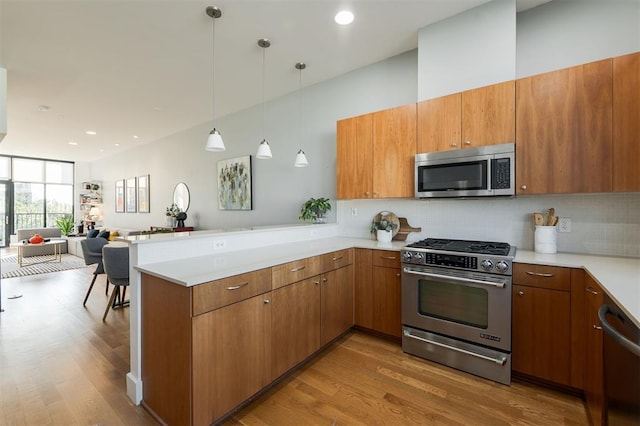 kitchen with kitchen peninsula, stainless steel appliances, decorative light fixtures, and hardwood / wood-style flooring