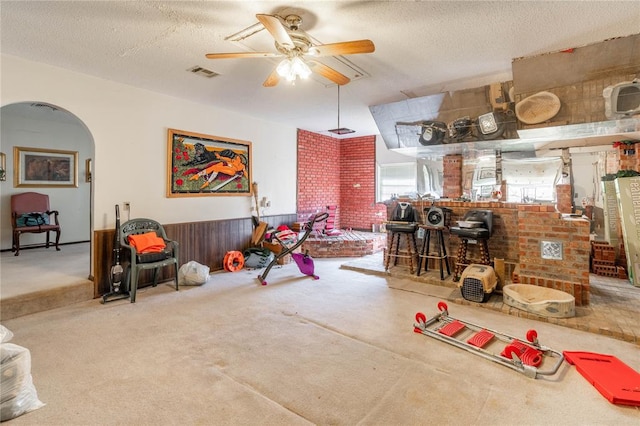 miscellaneous room with ceiling fan, carpet floors, a textured ceiling, bar, and wooden walls