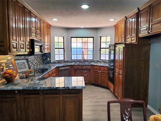 kitchen featuring sink, kitchen peninsula, dark stone countertops, black appliances, and light wood-type flooring