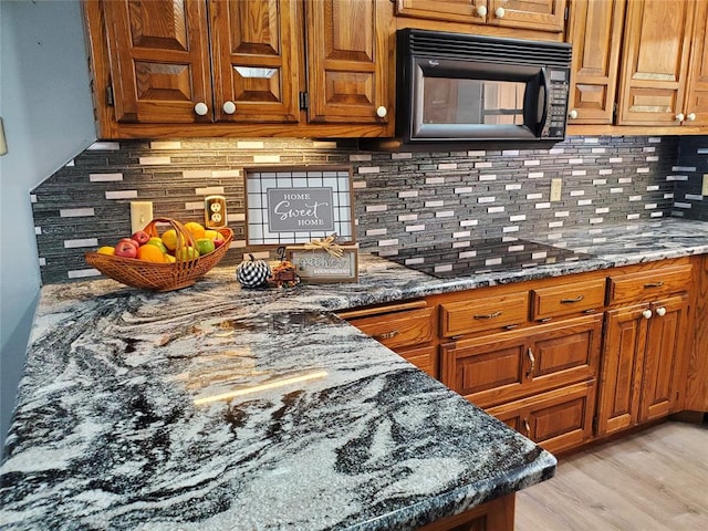 kitchen with backsplash, dark stone counters, and light wood-type flooring