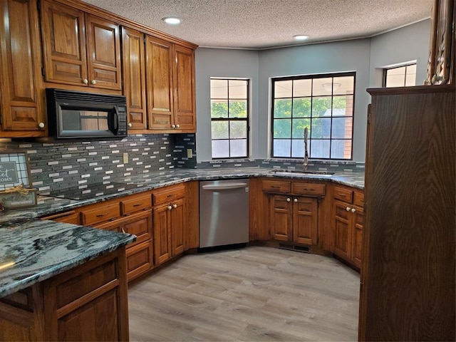 kitchen featuring dishwasher, sink, backsplash, light hardwood / wood-style floors, and dark stone counters