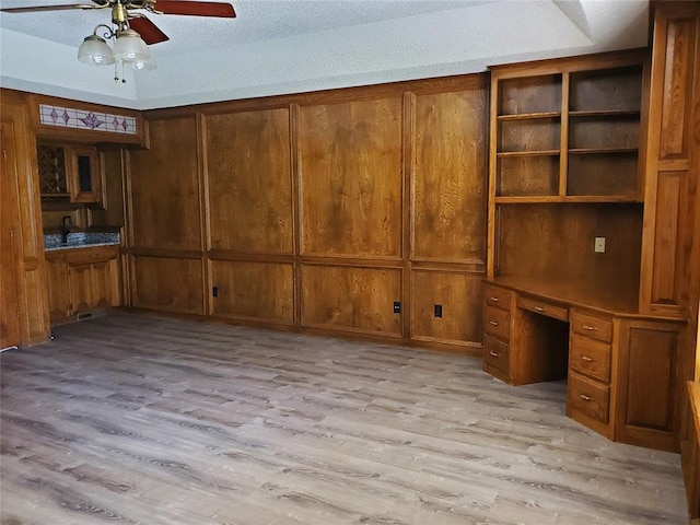 unfurnished office with ceiling fan, built in desk, a textured ceiling, and light hardwood / wood-style flooring