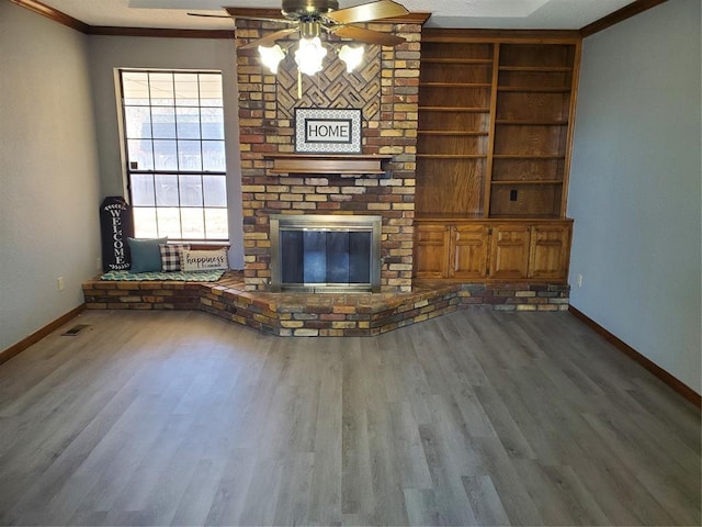 unfurnished living room featuring hardwood / wood-style flooring, a brick fireplace, ceiling fan, and crown molding