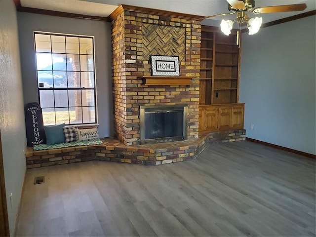 unfurnished living room featuring hardwood / wood-style floors, a brick fireplace, ceiling fan, and crown molding