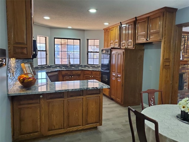 kitchen with kitchen peninsula, dishwasher, dark stone counters, and light hardwood / wood-style flooring