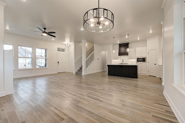 unfurnished living room with ceiling fan with notable chandelier, wood finish floors, a sink, stairway, and ornate columns