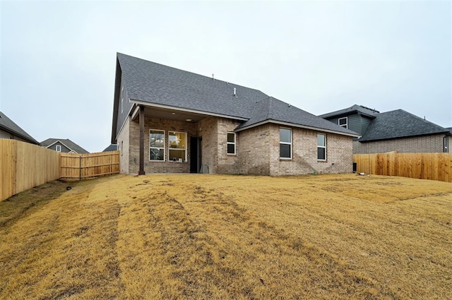 back of property featuring a yard, brick siding, a shingled roof, and a fenced backyard