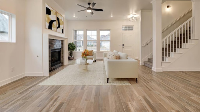 living area featuring a fireplace, stairs, light wood-style floors, and a healthy amount of sunlight