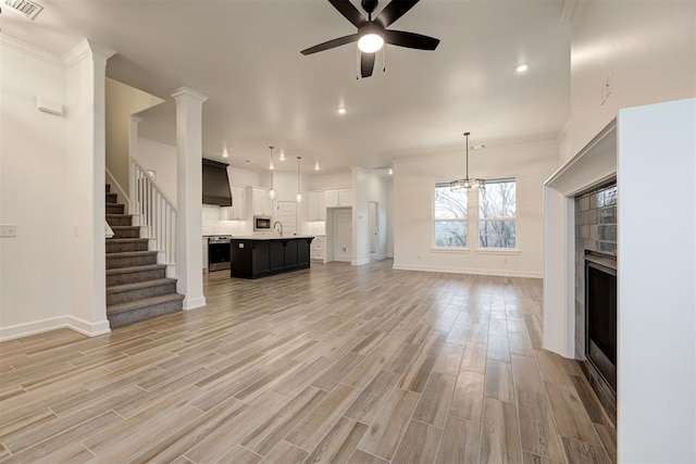 2348 Ridge Pine Rd, Edmond, OK 73034 - unfurnished living room with a tiled fireplace, ceiling fan, light wood-style flooring, stairs, and recessed lighting