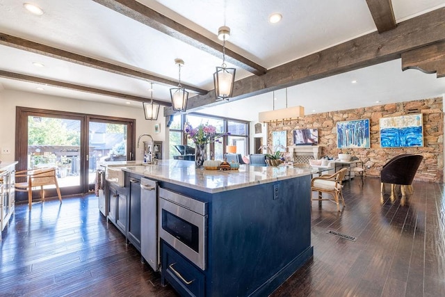 kitchen featuring stainless steel microwave, a center island with sink, hanging light fixtures, beam ceiling, and dark hardwood / wood-style flooring