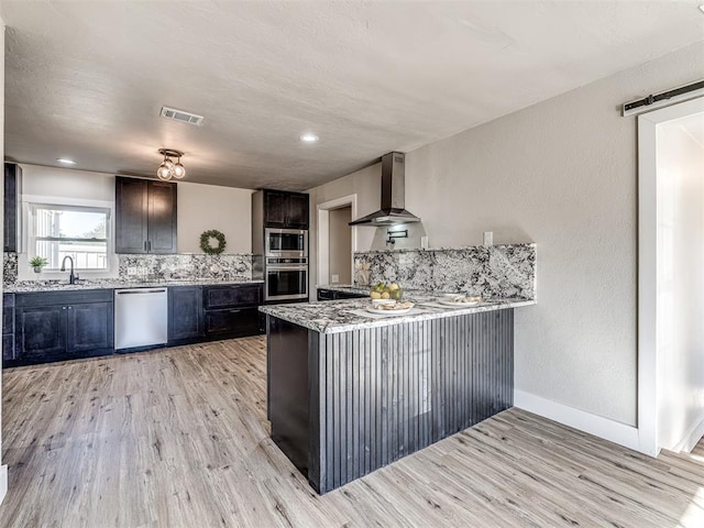 kitchen with sink, wall chimney exhaust hood, stainless steel appliances, light hardwood / wood-style flooring, and kitchen peninsula