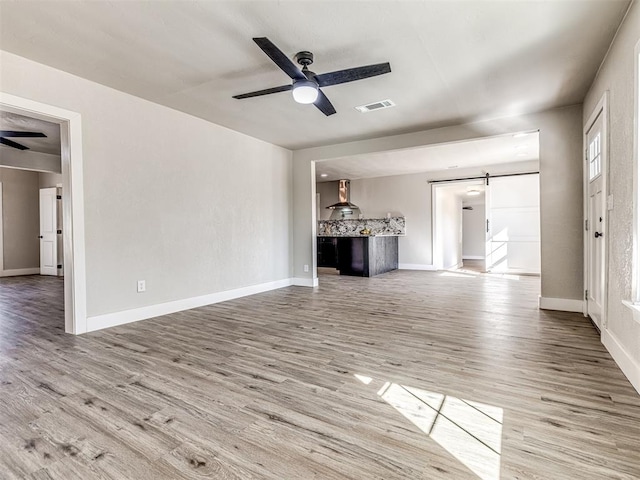 unfurnished living room with ceiling fan, a barn door, and light hardwood / wood-style floors