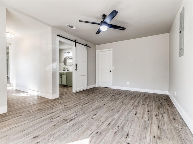 unfurnished bedroom with a barn door, ceiling fan, ensuite bathroom, and light wood-type flooring