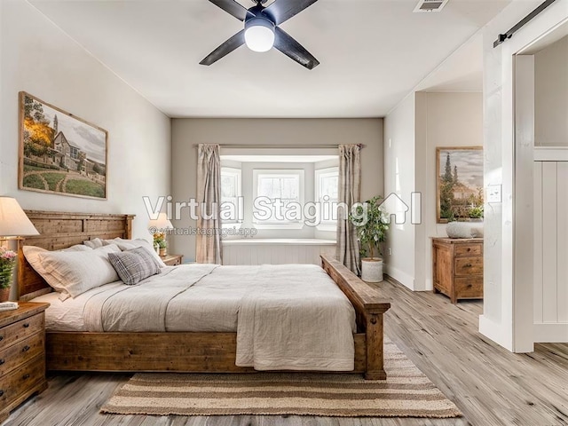 bedroom featuring light wood-type flooring, ceiling fan, and a barn door