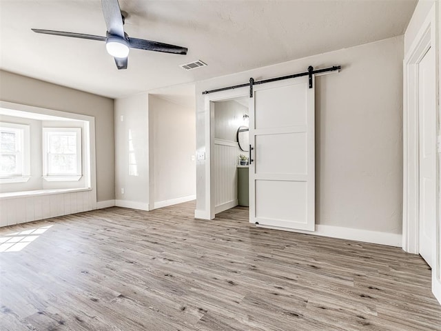 unfurnished bedroom with ceiling fan, a barn door, and light hardwood / wood-style floors