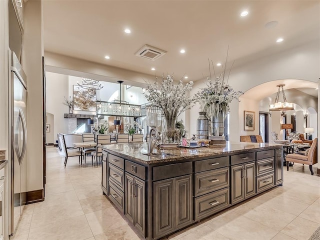 kitchen featuring dark brown cabinets, sink, light tile patterned floors, decorative light fixtures, and dark stone countertops