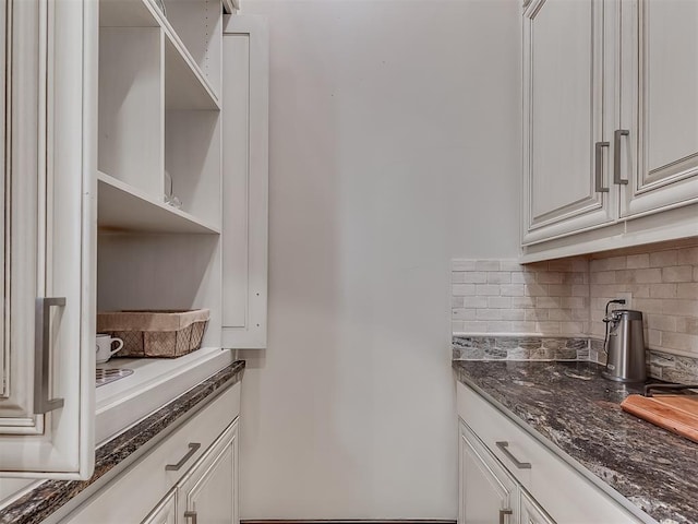 kitchen featuring backsplash, white cabinetry, and dark stone counters