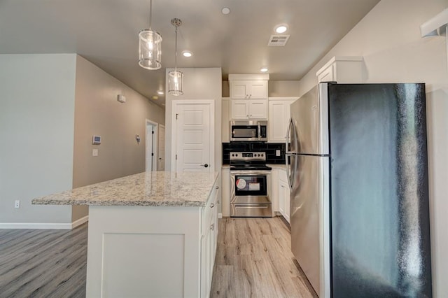 kitchen with light hardwood / wood-style flooring, light stone countertops, appliances with stainless steel finishes, a kitchen island, and white cabinetry