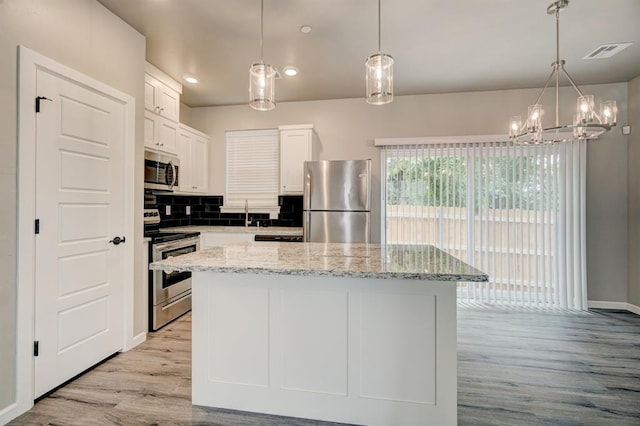 kitchen featuring appliances with stainless steel finishes, tasteful backsplash, a center island, light hardwood / wood-style floors, and white cabinetry