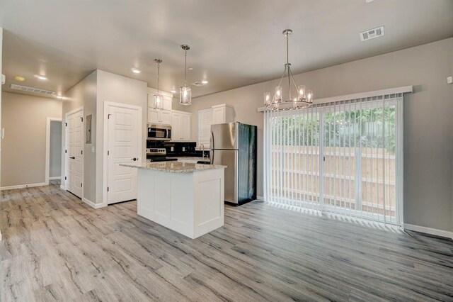 kitchen with a kitchen island, white cabinets, hanging light fixtures, and appliances with stainless steel finishes