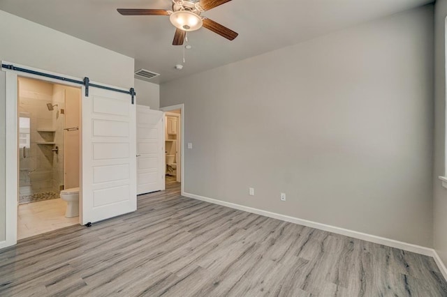 unfurnished bedroom featuring a barn door, ceiling fan, ensuite bathroom, and light hardwood / wood-style floors