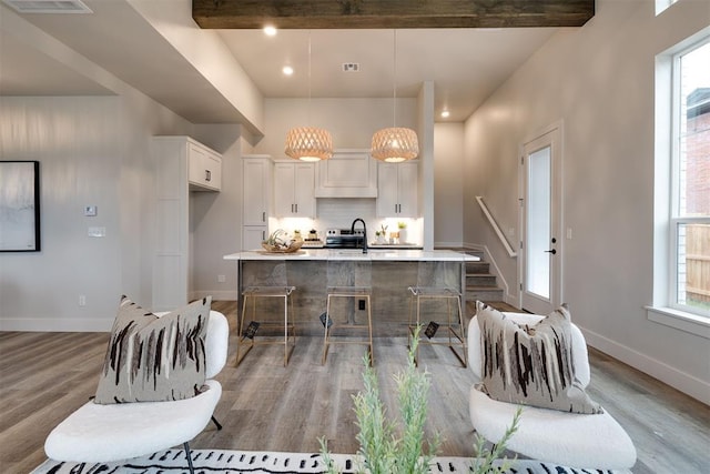 kitchen with white cabinets, pendant lighting, a center island with sink, and light wood-type flooring