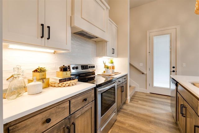 kitchen featuring appliances with stainless steel finishes, tasteful backsplash, premium range hood, light hardwood / wood-style flooring, and white cabinets