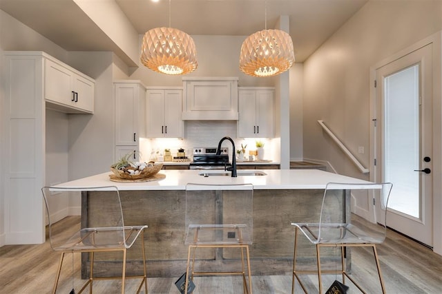 kitchen featuring hanging light fixtures, light hardwood / wood-style flooring, an island with sink, a kitchen bar, and white cabinetry