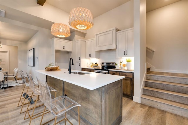 kitchen with pendant lighting, stainless steel electric range, a kitchen island with sink, white cabinets, and light hardwood / wood-style floors