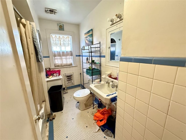 bathroom featuring heating unit, sink, tile walls, tile patterned flooring, and toilet