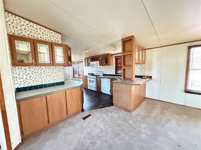 kitchen featuring white appliances, a peninsula, a healthy amount of sunlight, visible vents, and glass insert cabinets