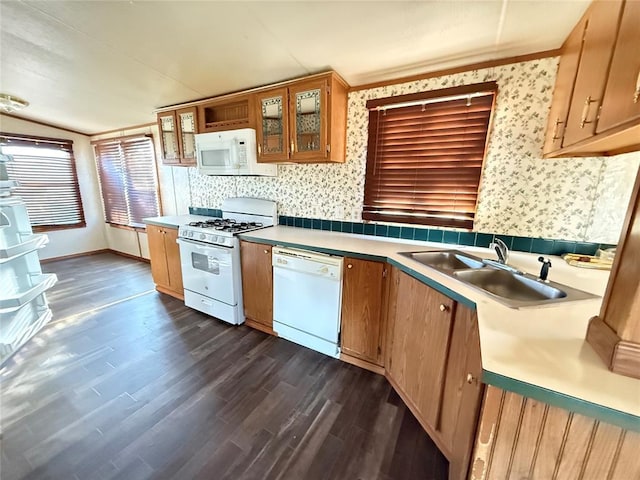 kitchen with a sink, white appliances, light countertops, dark wood finished floors, and wallpapered walls