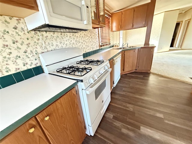 kitchen featuring dark wood finished floors, brown cabinets, a sink, wallpapered walls, and white appliances