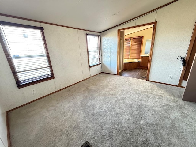 unfurnished bedroom with crown molding, ensuite bath, carpet, baseboards, and vaulted ceiling