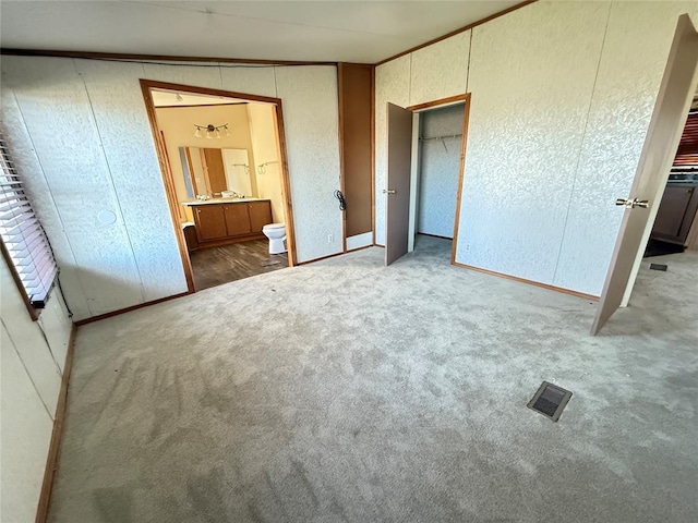 unfurnished bedroom with visible vents, carpet floors, baseboards, connected bathroom, and a textured wall