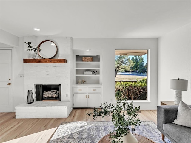 living room with built in shelves, a brick fireplace, and light hardwood / wood-style flooring