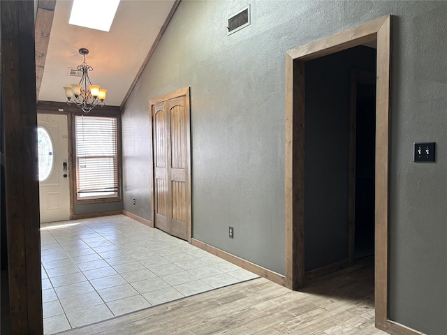 foyer entrance with light wood-type flooring, an inviting chandelier, ornamental molding, and lofted ceiling with skylight