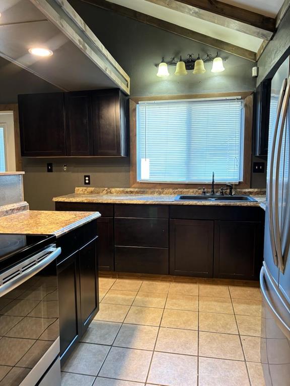 kitchen with light tile patterned floors, appliances with stainless steel finishes, sink, and vaulted ceiling with beams